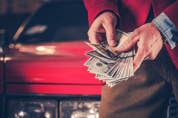Close-up of a man counting his money in front of his red car